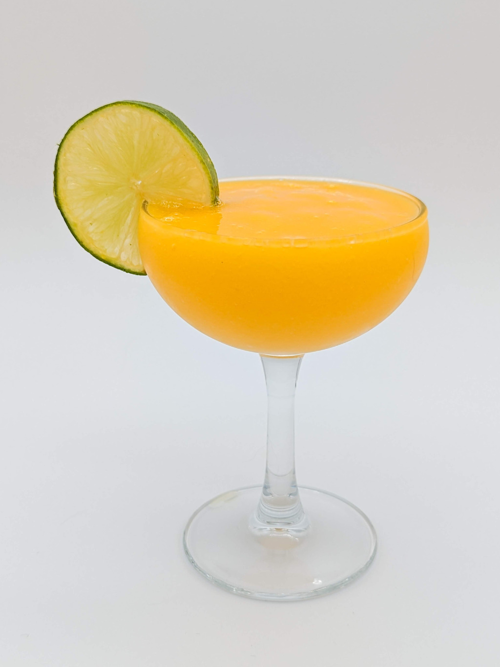 Bright orange liquid in a coupe glass with a lime wheel garnish