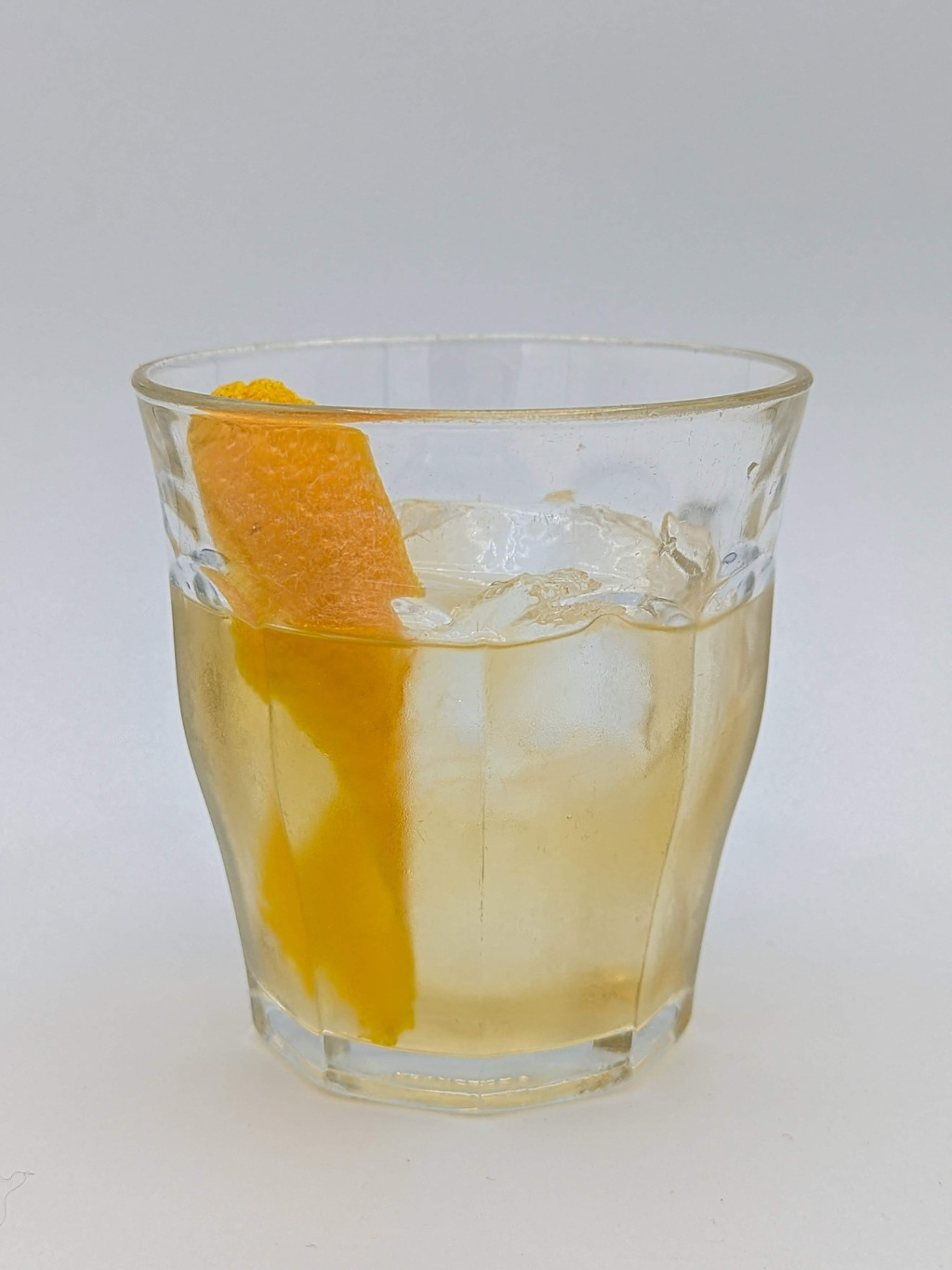 Straw colored liquid in an old fashioned glass filled with ice and with a orange peel garnish