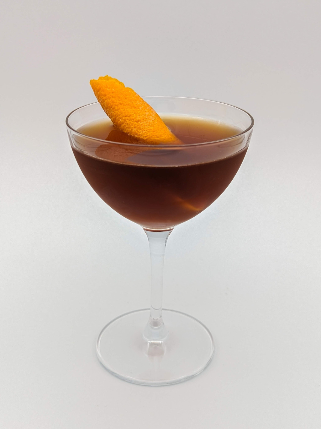 orange brown liquid in a coupe with an orange peel garnish