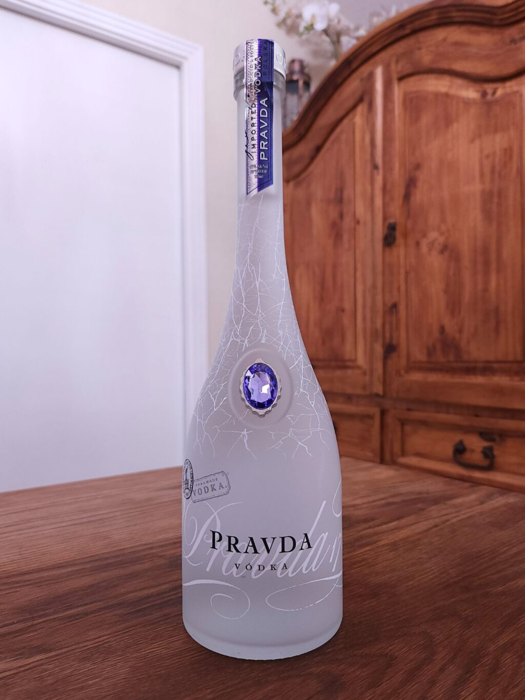 Bottle of Pravda Vodka sitting on a wooden table, in front of a mixed white and wooden background
