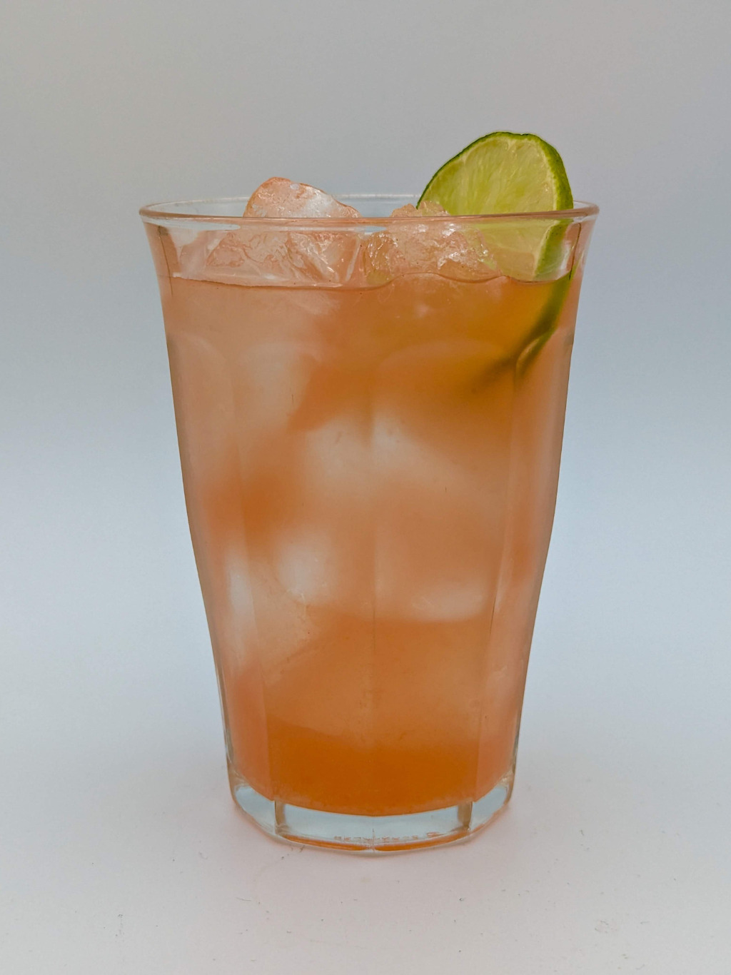 pink liquid in a tall glass with a lime wheel garnish