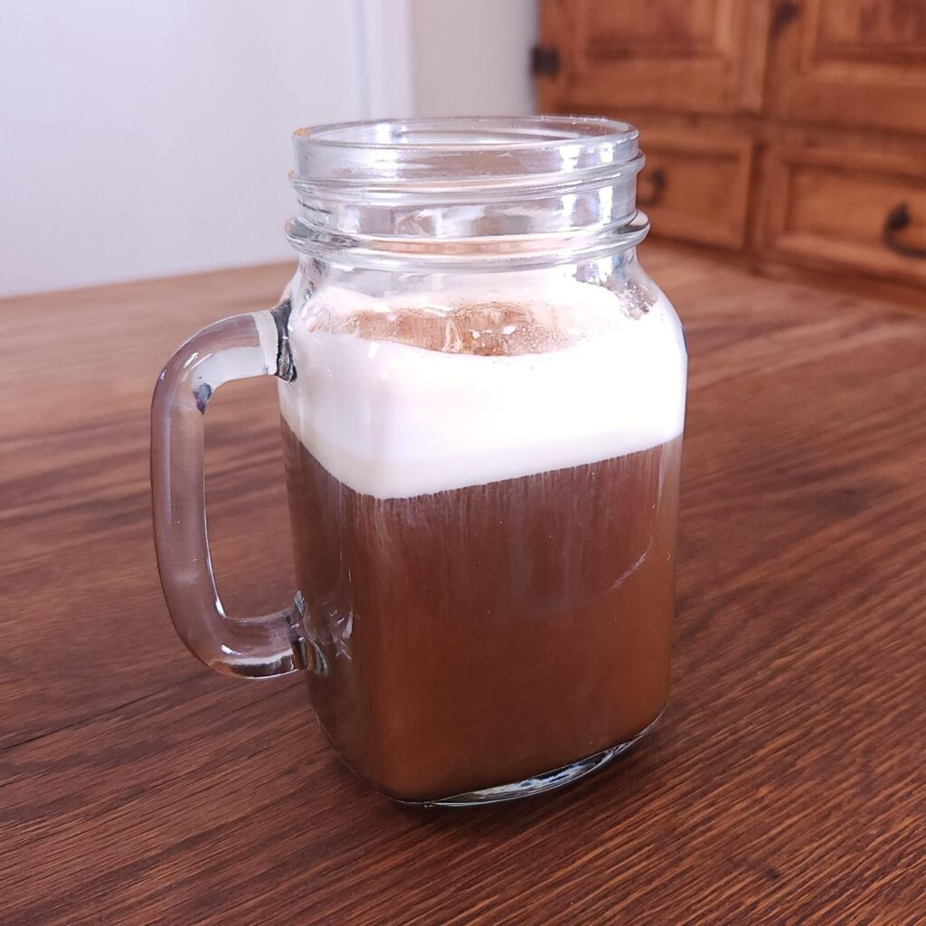 glass mug filled with opaque brown liquid that is topped with foamy whipped cream and powdered cinnamon