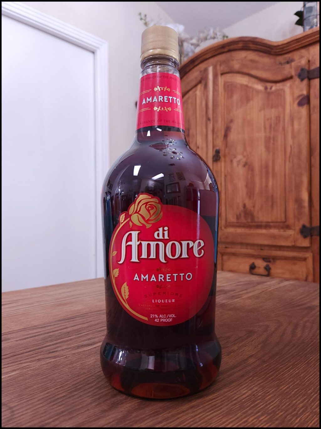 bottle of Di Amore Amaretto sitting on a wooden table, in front of a mixed white and wooden background