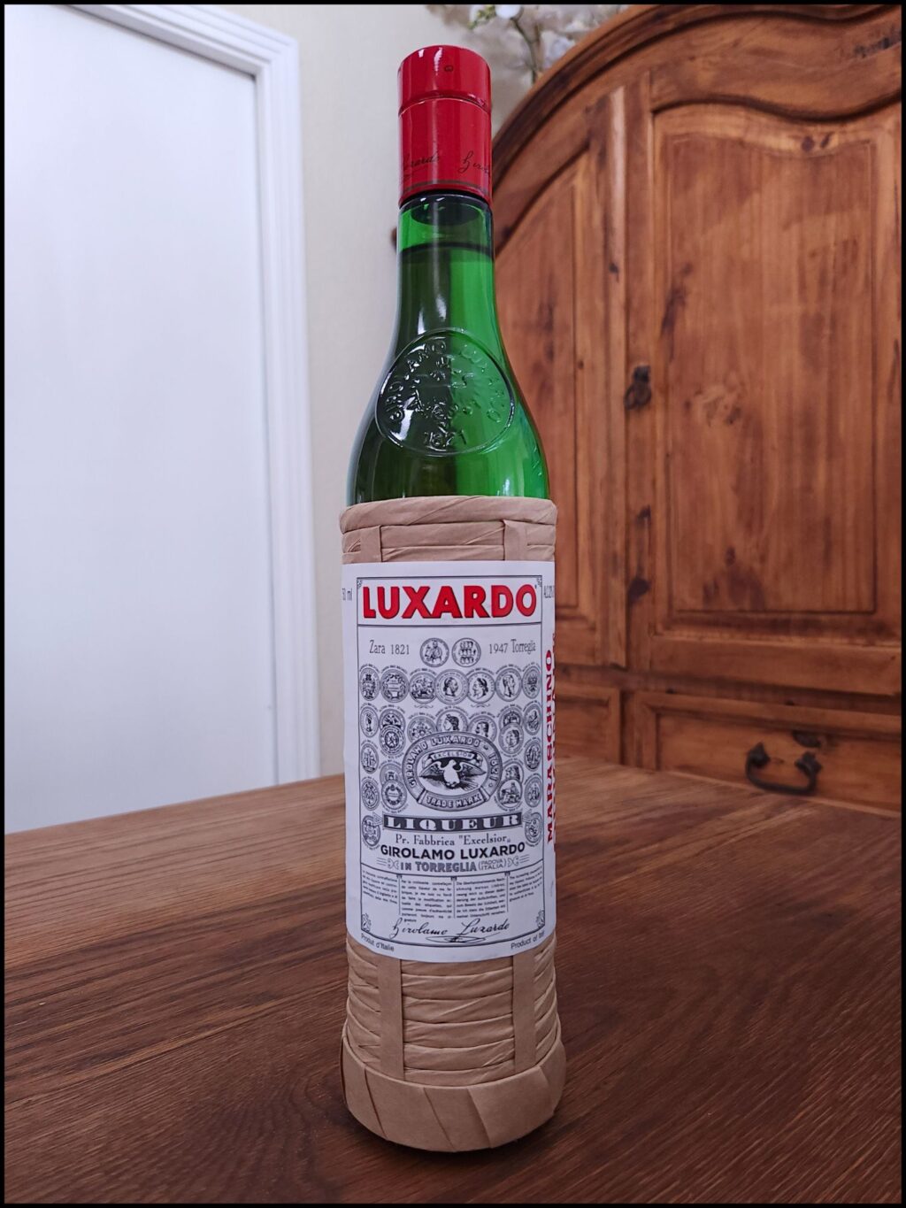 bottle of Luxardo Maraschino Liqueur sitting on a wooden table, in front of a mixed white and wooden background