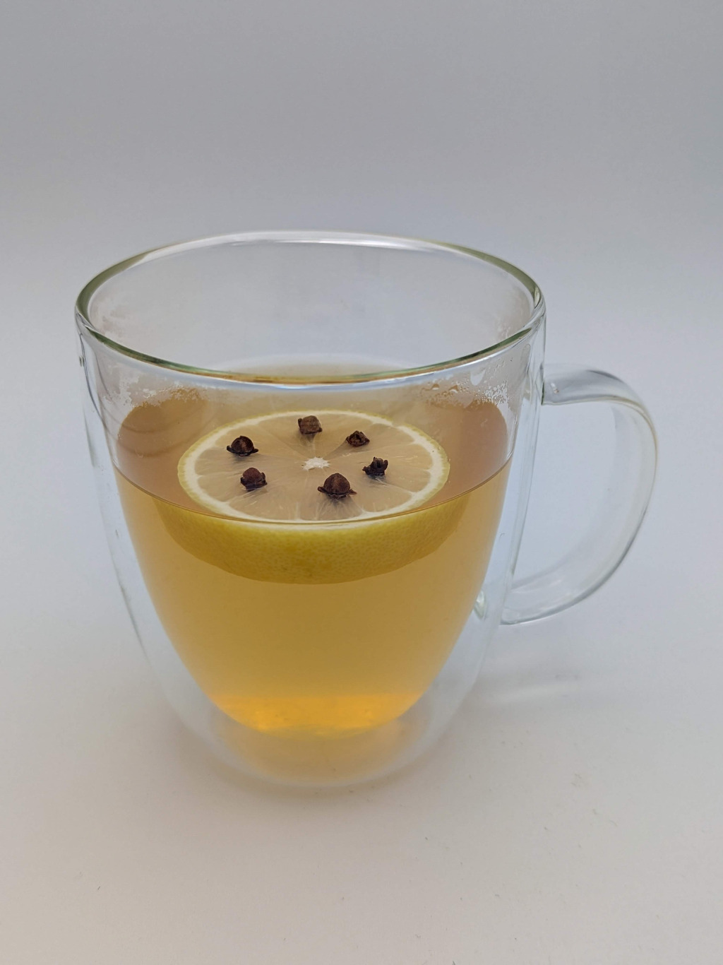 Light Gold liquid in a glass mug with a lemon wheel and clove garnish