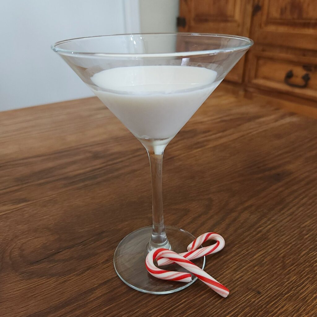 Martini glass halfway filled with creamy white liquid, sitting on a wooden table with two small candy canes strewn artistically below the stem