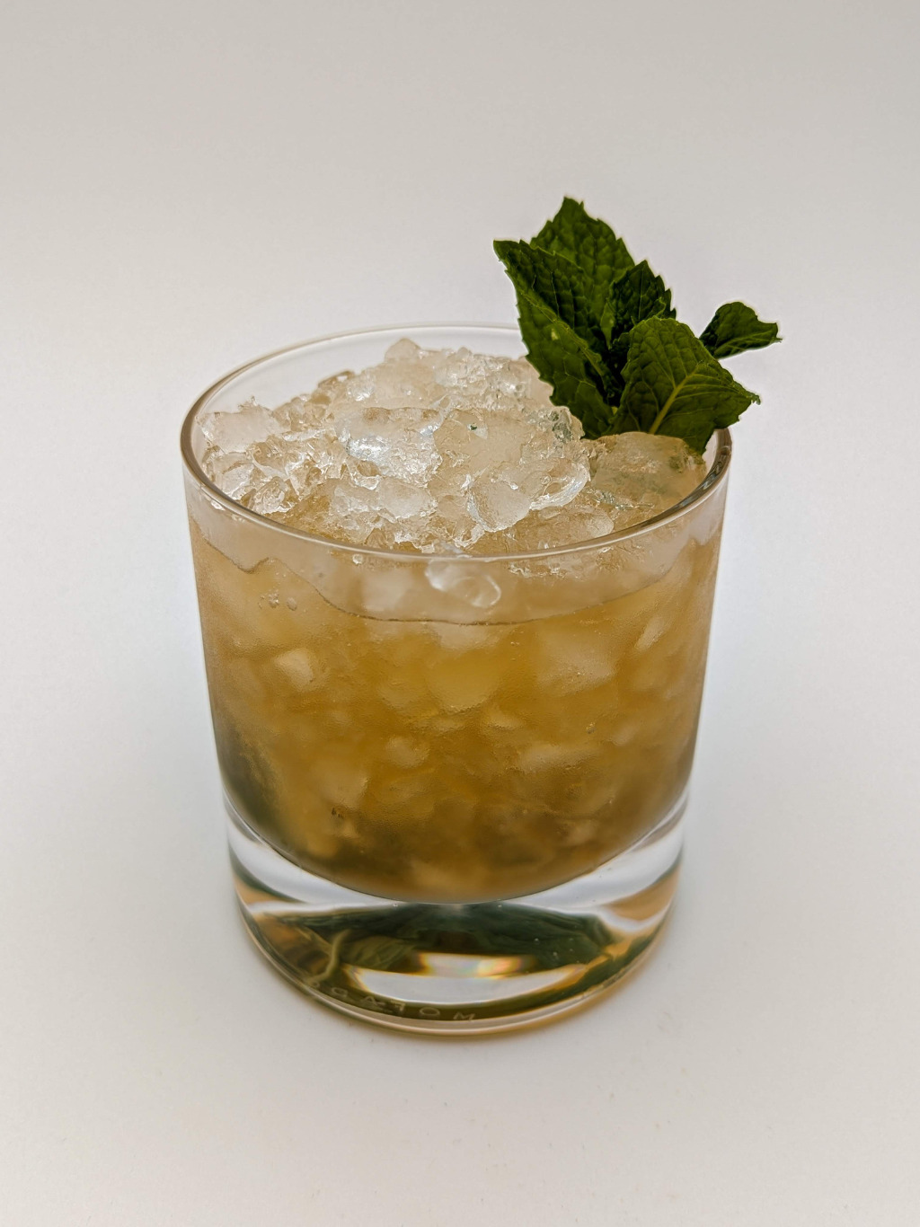 Golden brown liquid in a rocks glass filled with crushed ice with a mint sprig garnish