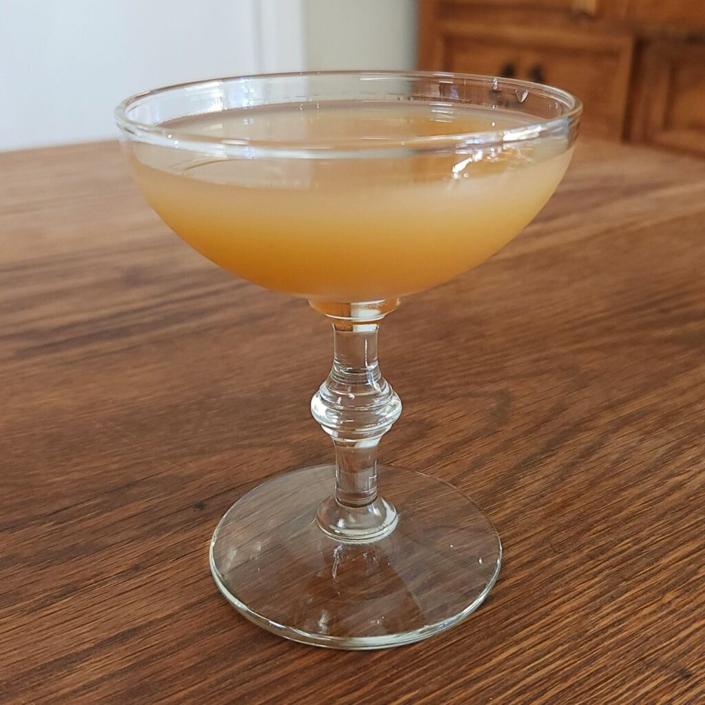 Coupe glass filled with cloudy golden liquid, sitting on a wooden table