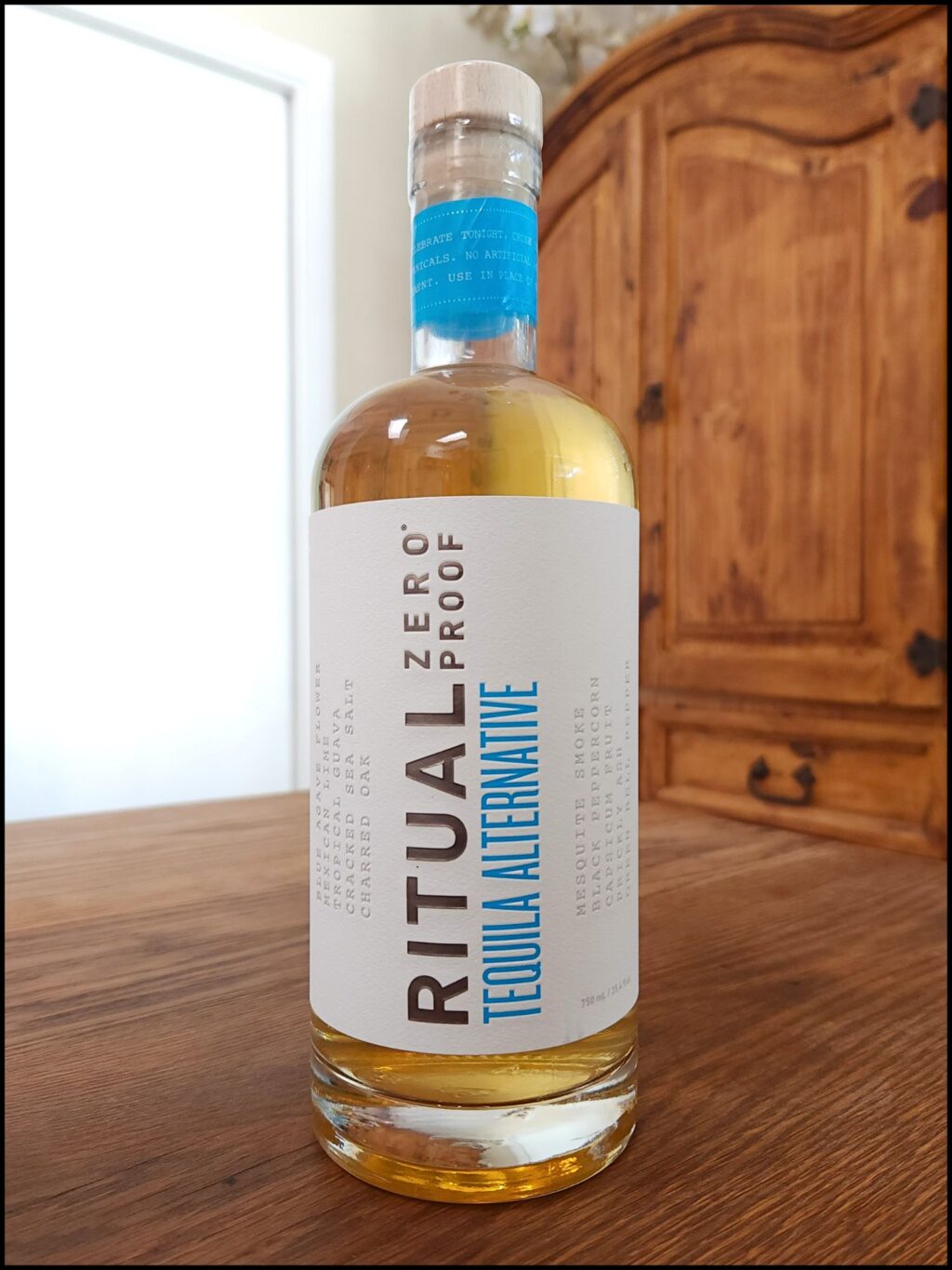 Bottle of Ritual Zero Proof Tequila alternative sitting on a wooden table, in front of a mixed white and wooden background