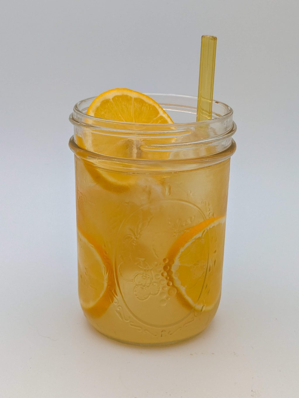 gold liquid in a glass jar filled with ice garnished with lemon wheels
