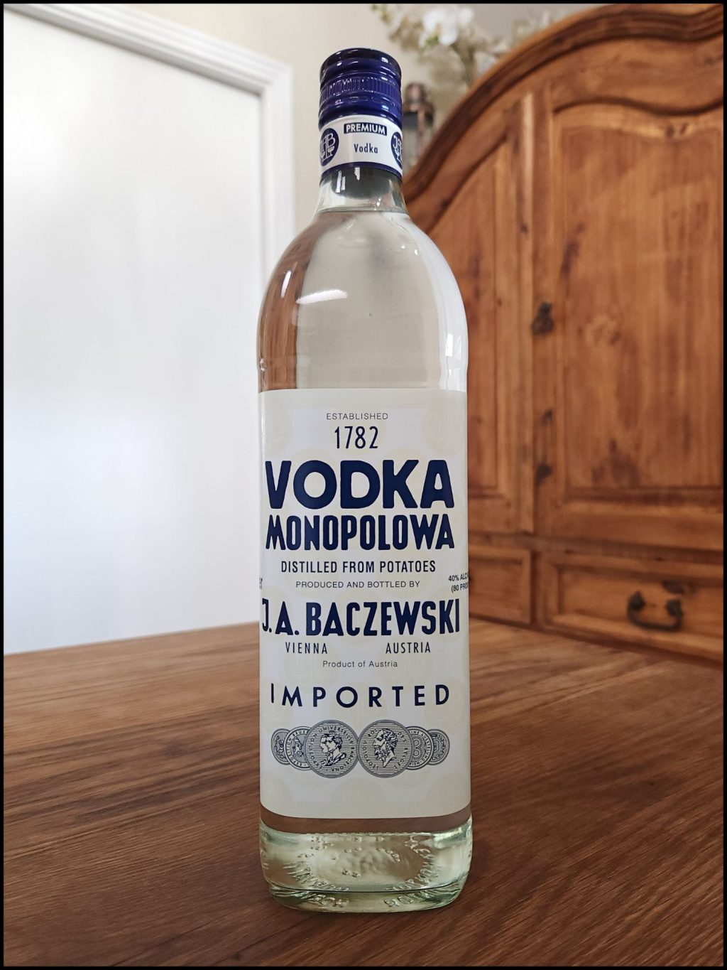 Bottle of Monopolowa Vodka sitting on a wooden table, in front of a mixed white and wooden background