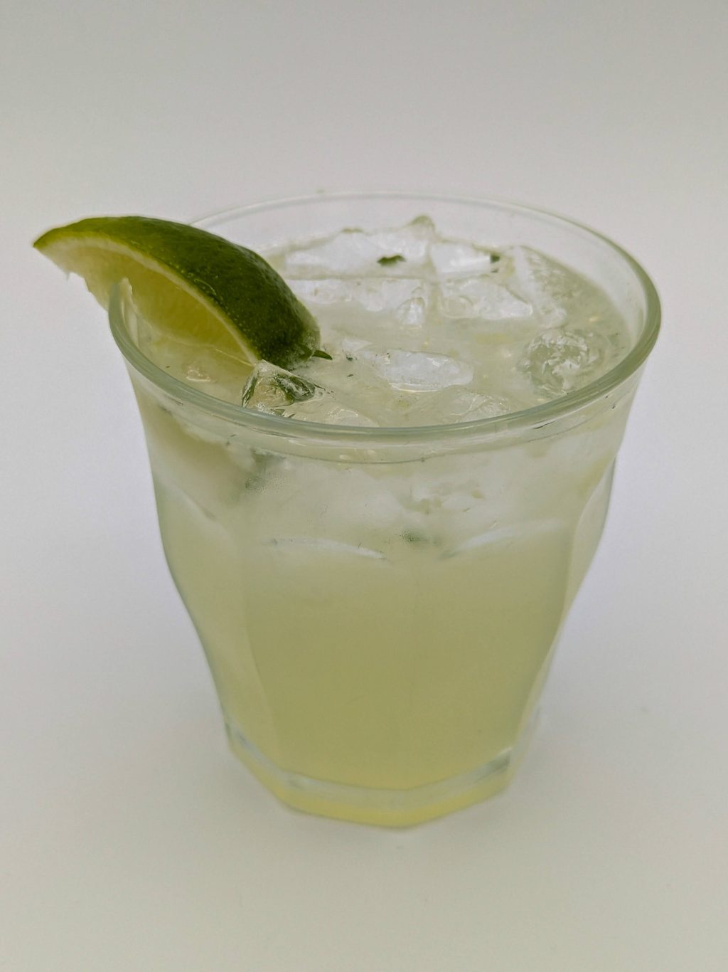 light green liquid in a glass filled with ice and garnished with a lime wedge