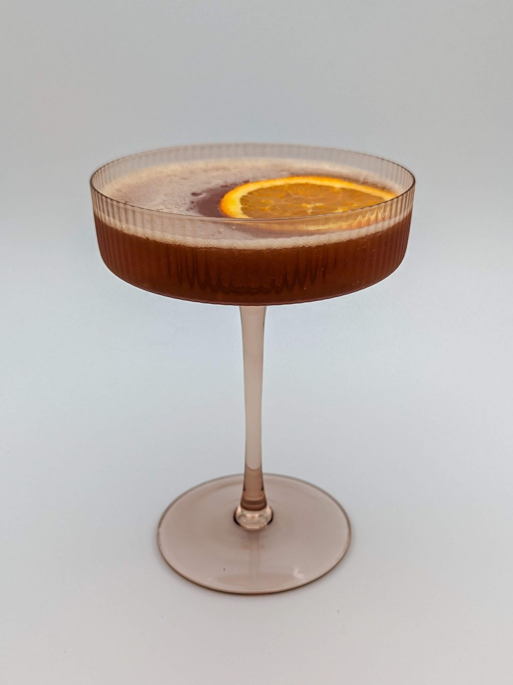 Reddish brown liquid in a martini glass with a orange wheel garnish