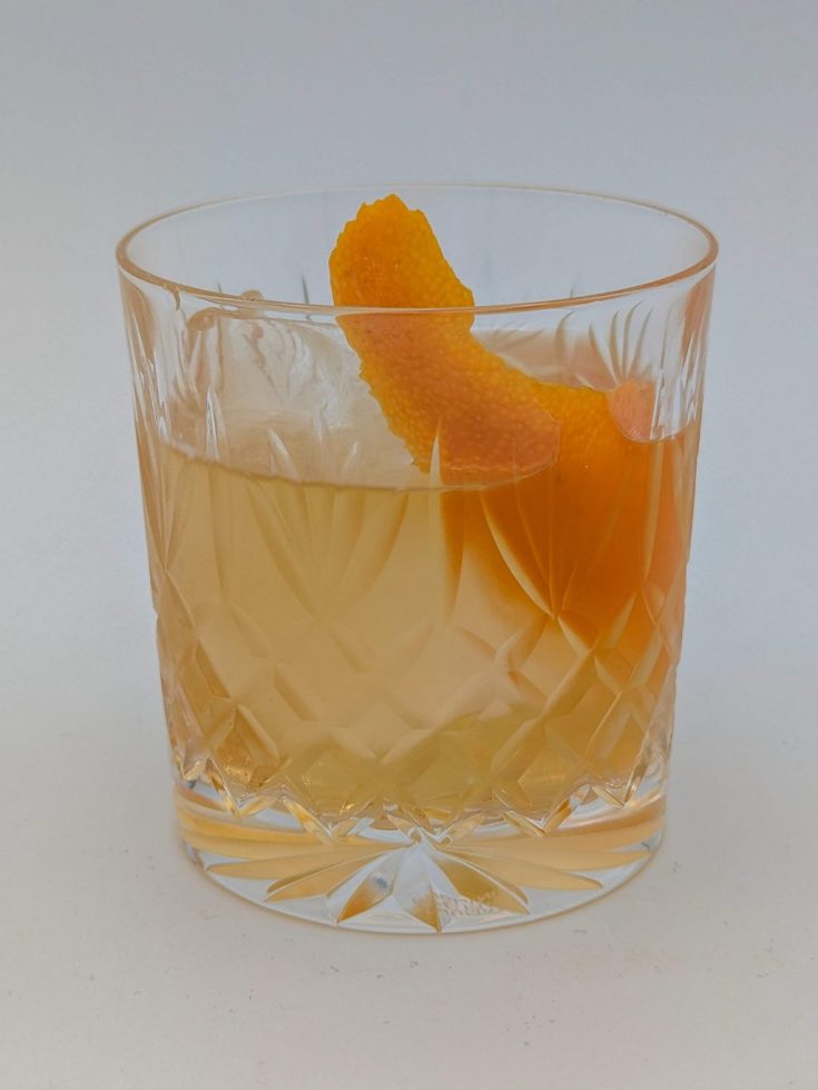 gold liquid in an ornate glass with a orange peel garnish