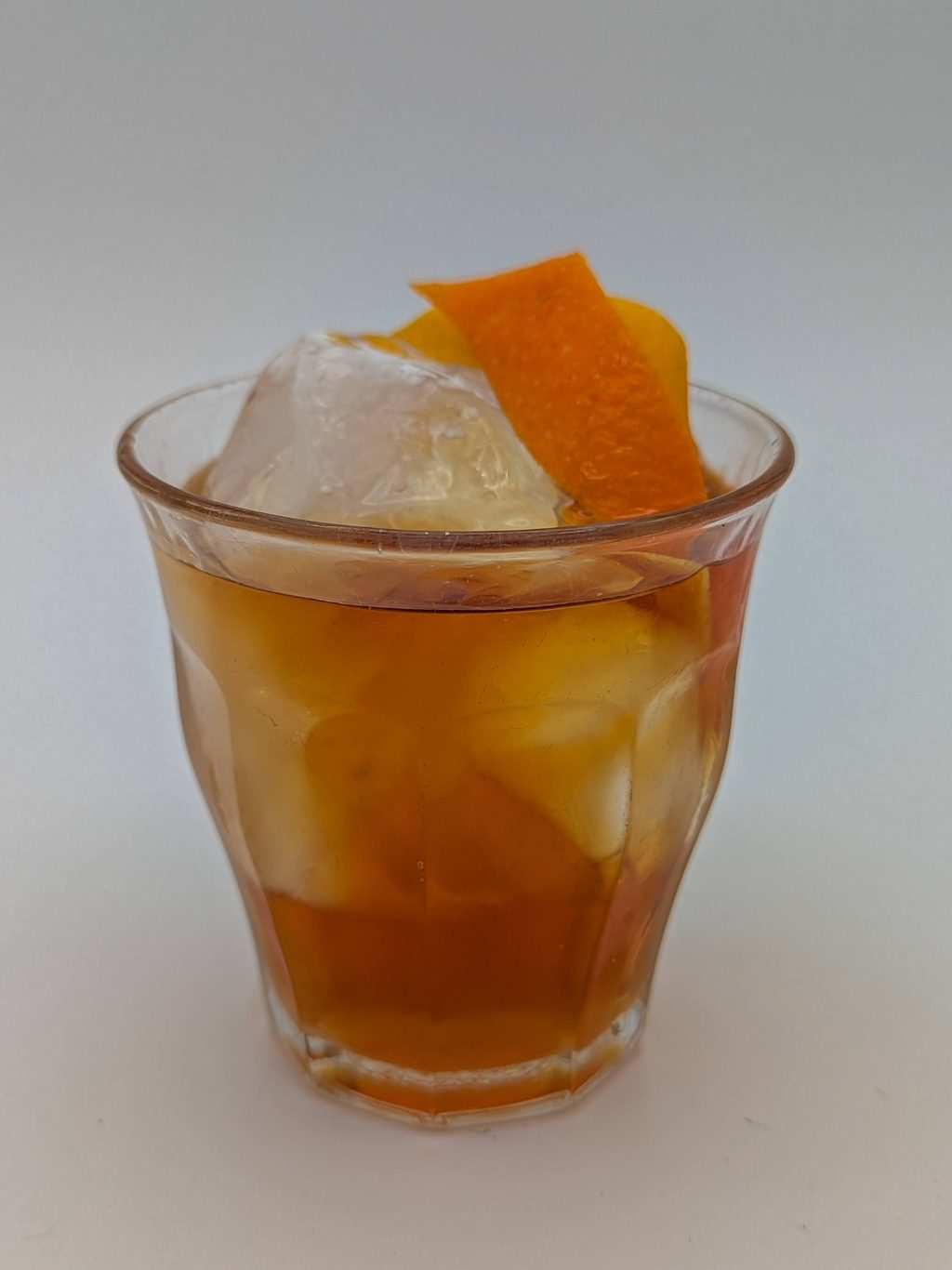 Amber liquid and a large ice cube in an old fashioned glass with a lemon and orange peel garnish