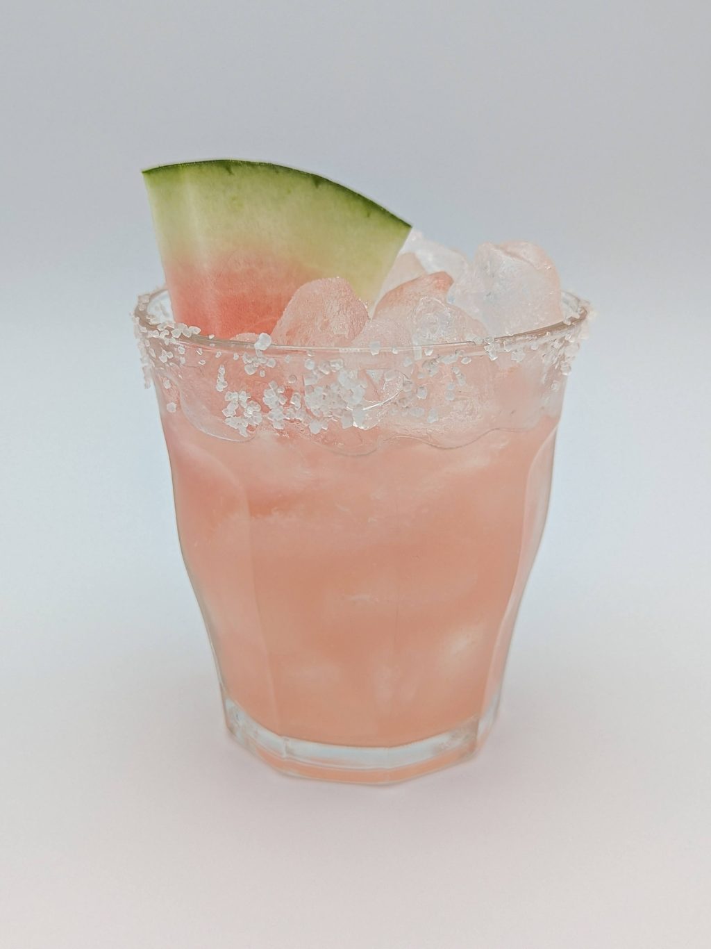 pink liquid in an old fashioned glass filled with ice and garnished with a watermelon slice and salt rim