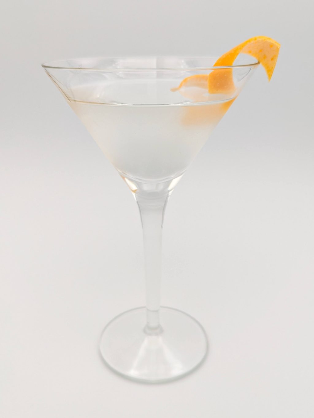 clear liquid in a martini glass with a grapefruit peel garnish