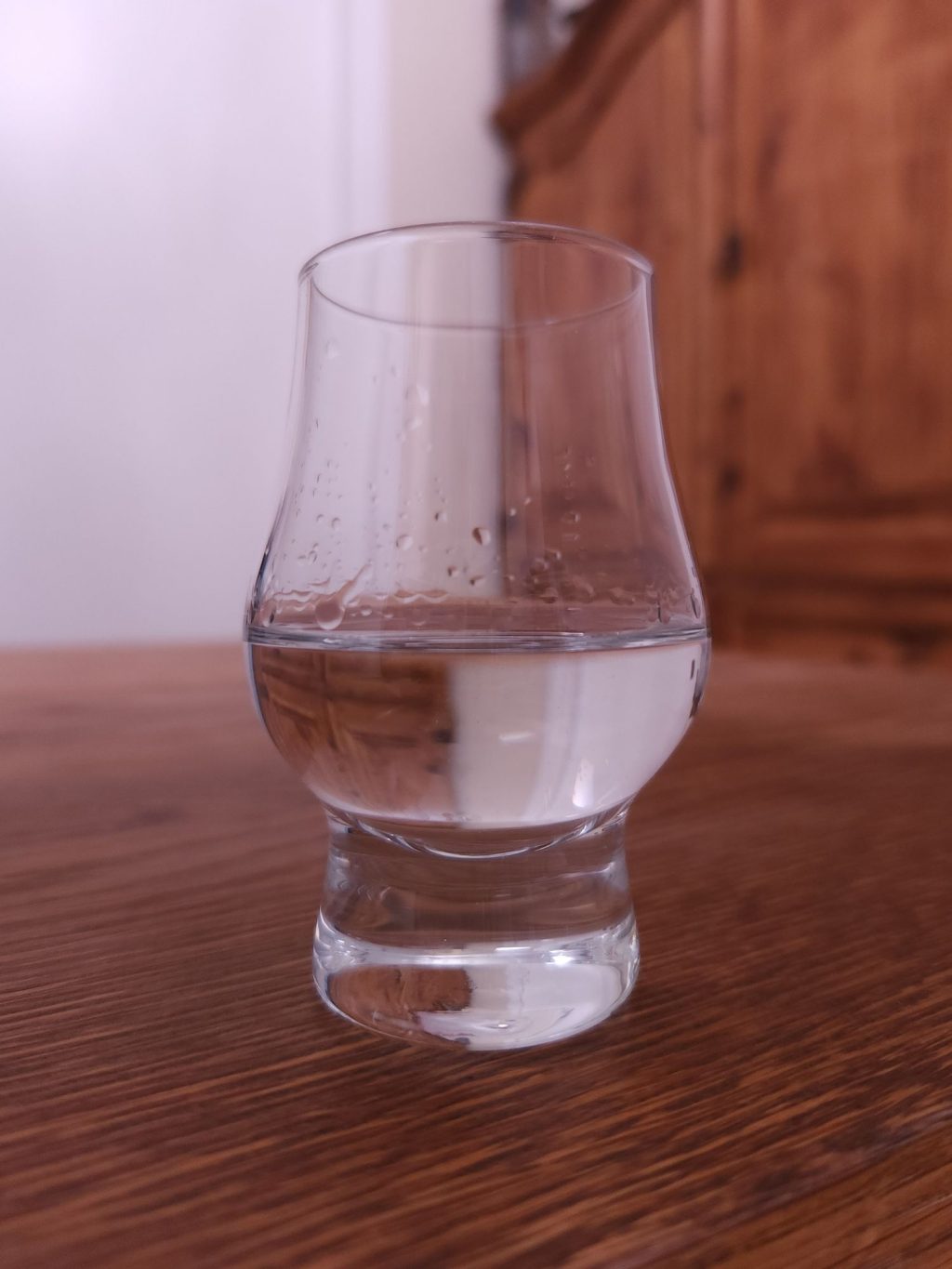 Small glencairn glass with clear liquid, sitting on a wooden table