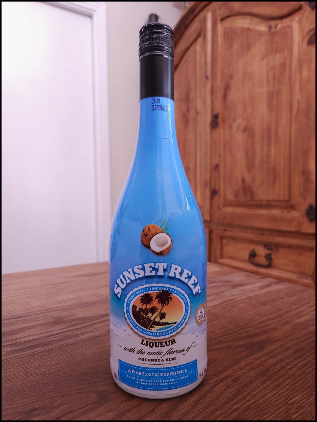 Bottle of Sunset Reef Coconut Rum with a bright light blue and while label design, and a black cap