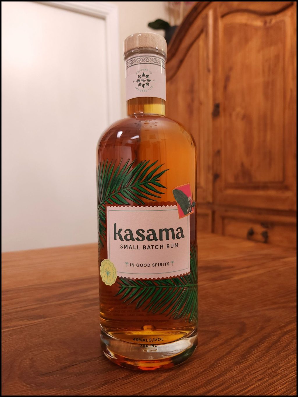 Bottle of Kasama Small Batch Rum with golden brown liquid and an off-white and green label design, sitting on a wooden table