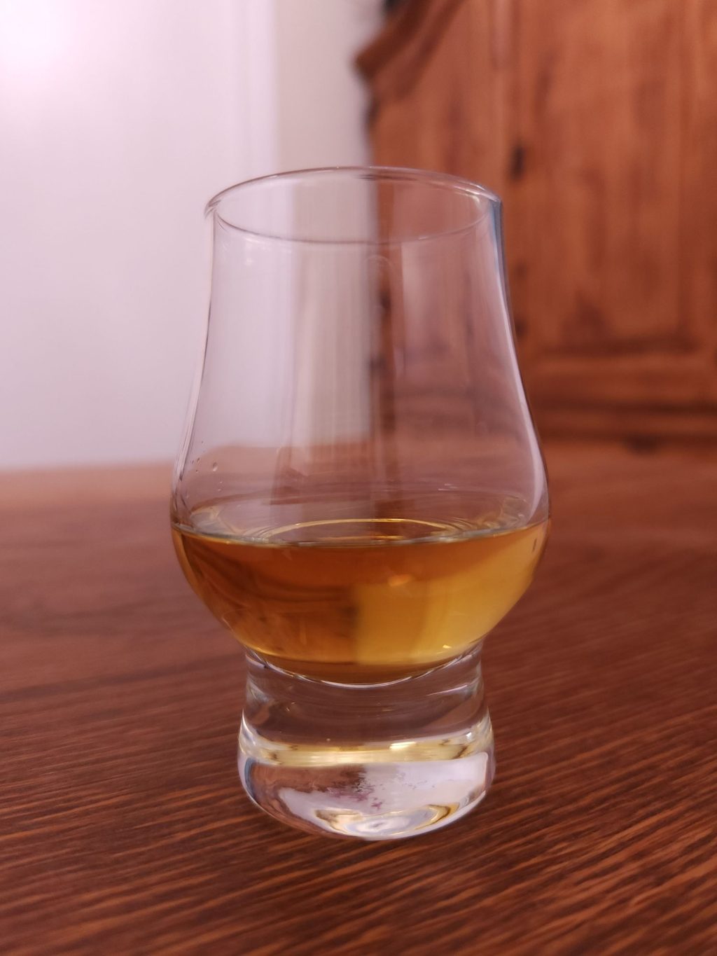 Small glencairn glass with golden brown liquid, sitting on a wooden table