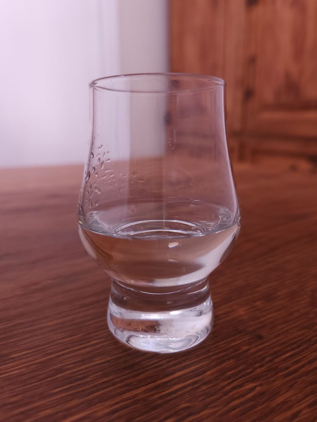Glencairn glass with clear liquid, sitting on a wooden table.
