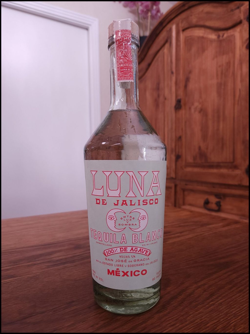 Bottle of Luna de Jalisco Blanco Tequila with a light blue and red label design, sitting on a wooden table