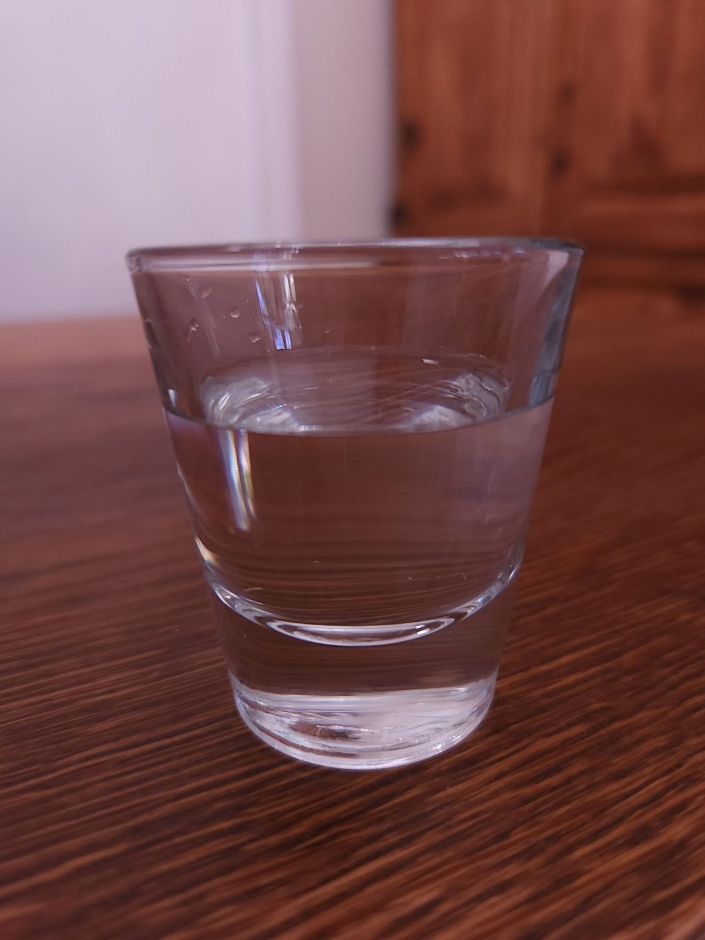 Shot glass with clear liquid, sitting on a wooden table