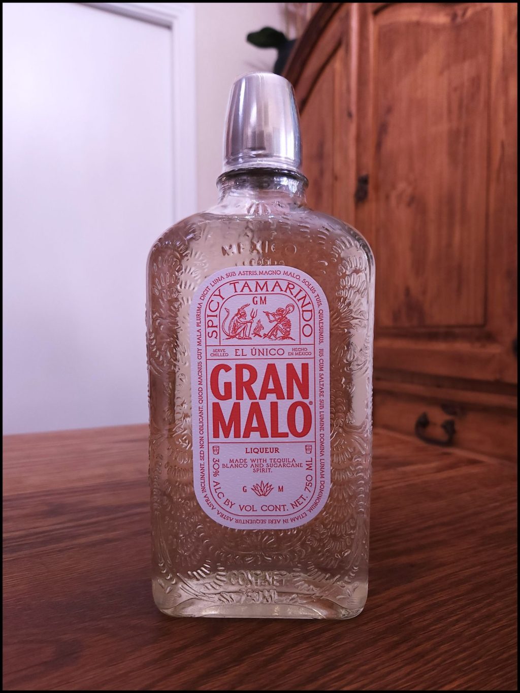 Bottle of Gran Malo Tamarindo with yellowish clear liquid, a red and white label design, and a metal shot glass top