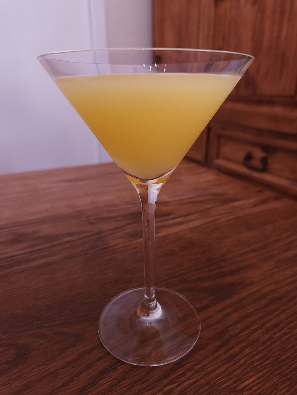 Martini glass filled with bright yellow liquid, sitting on a wooden table