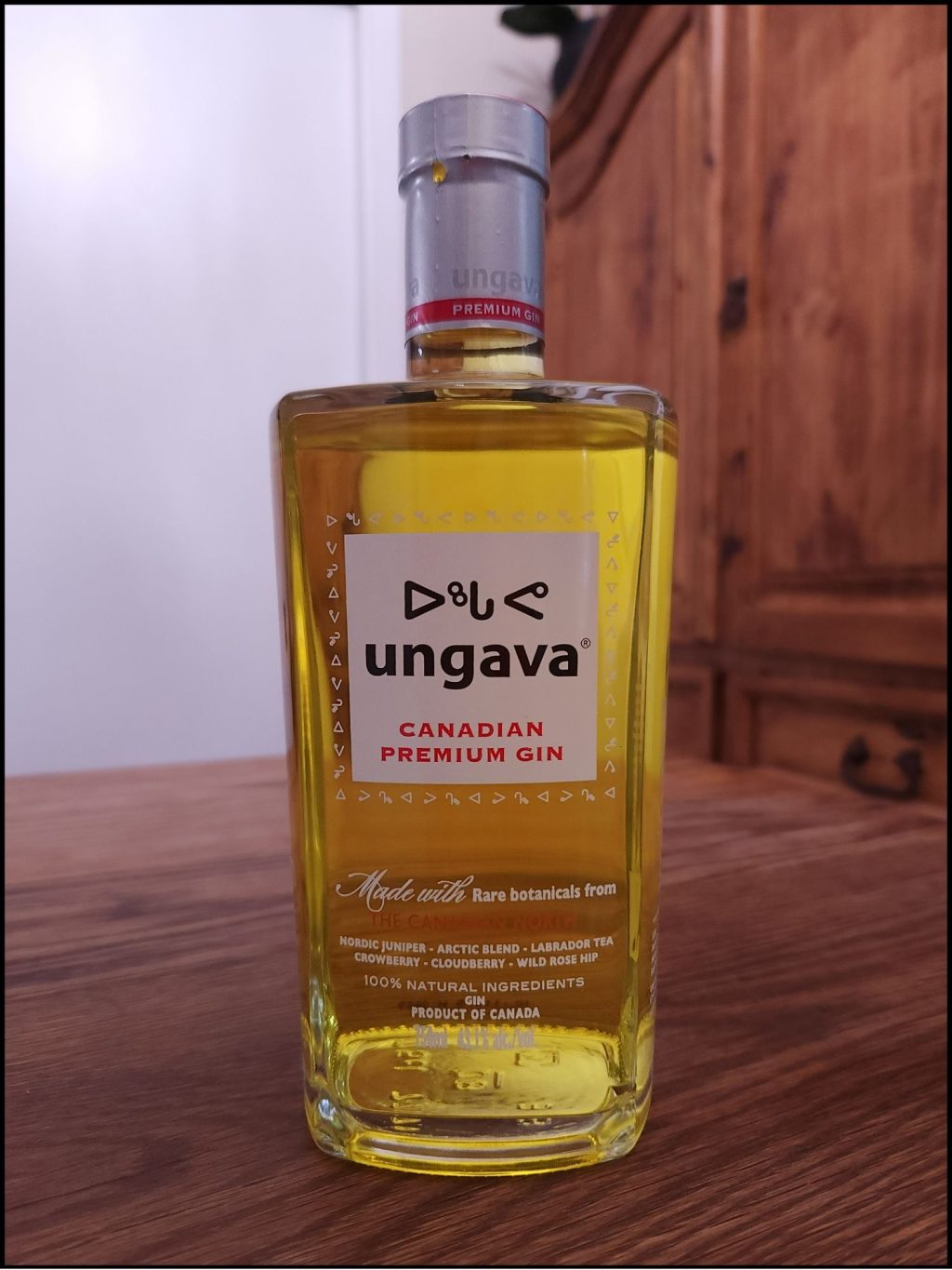 Bottle of Ungava Gin with bright yellow liquid and a white, black, and red label design, sitting on a wooden table