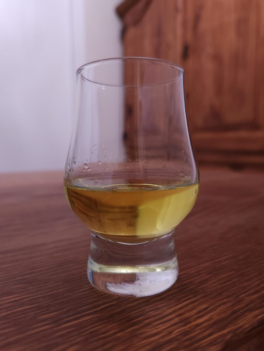 Small glencairn glass with bright yellow liquid, sitting on a wooden table