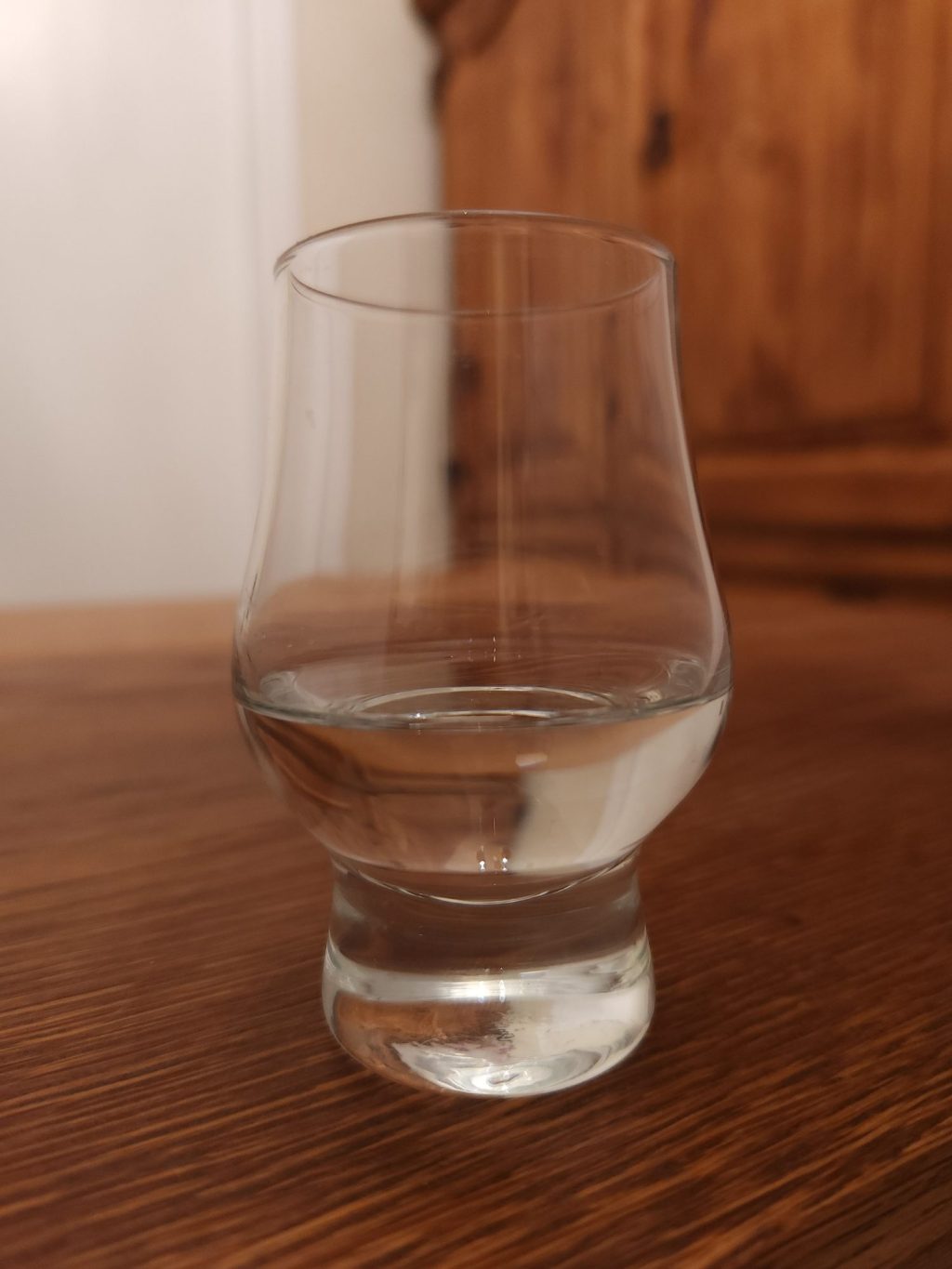 Small glencairn glass with clear liquid, sitting on a wooden table