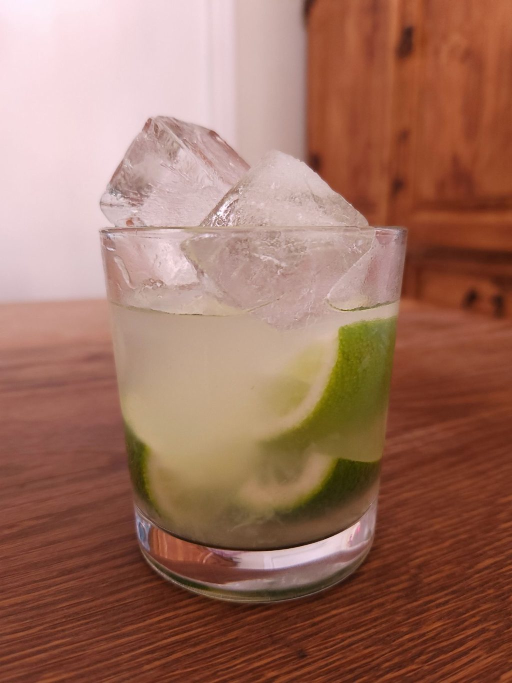 Rocks glass filled with very light green liquid, squeezed out lime wedges, and large ice cubes