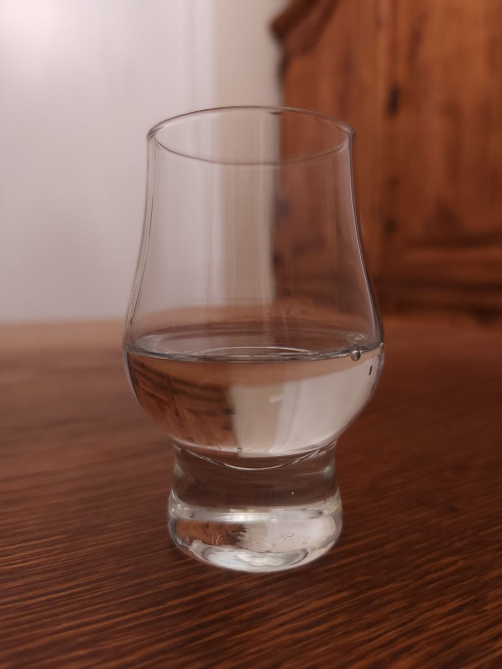 Small glencairn glass with clear liquid, sitting on a wooden table