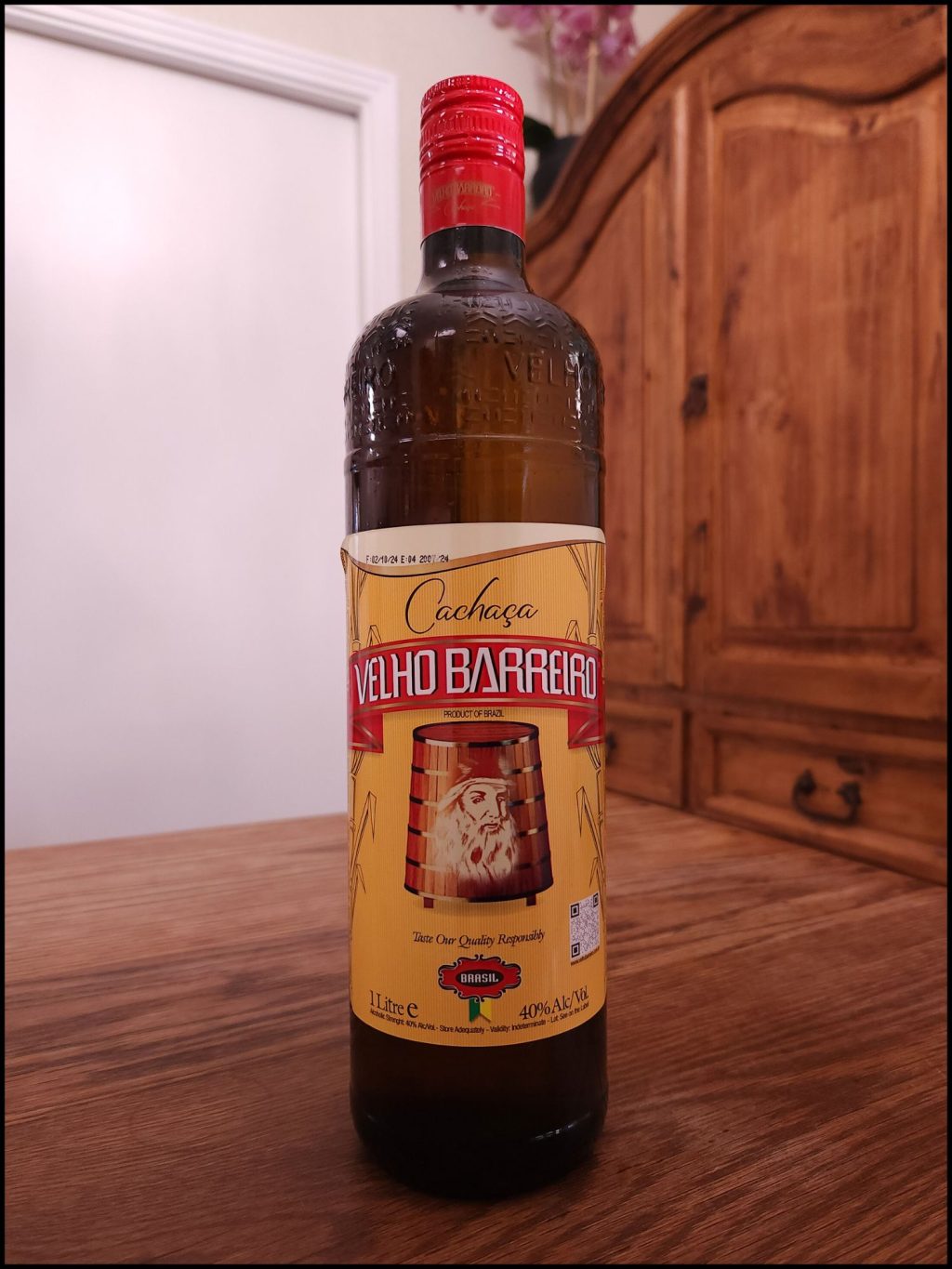 Tall bottle with dark brown glass and a bright yellow and red label design, sitting on a wooden table