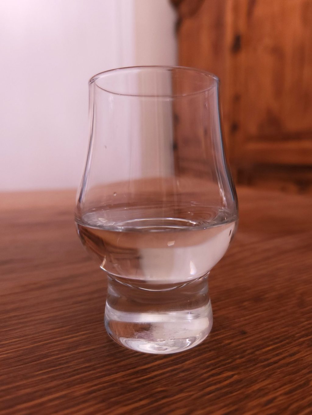 Small glencairn glass with clear liquid, sitting on a wooden table