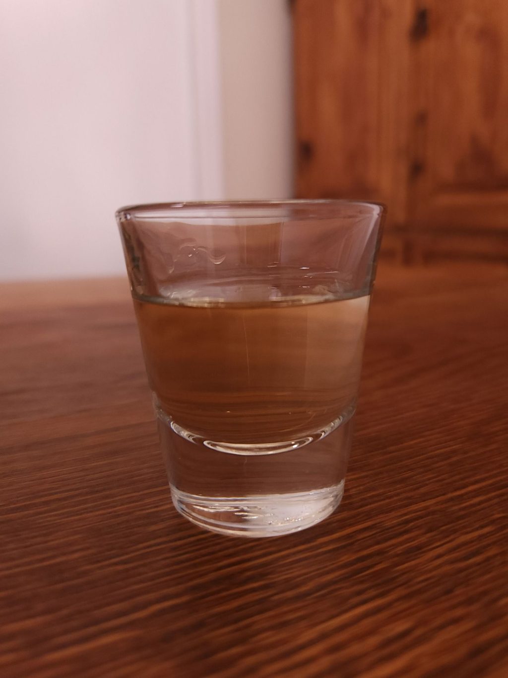 Shot glass with light amber liquid, sitting on a wooden table