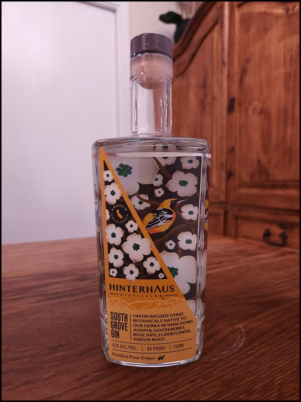 Glass bottle with an artistic floral design label in yellow, brown, and white, sitting on a wooden table