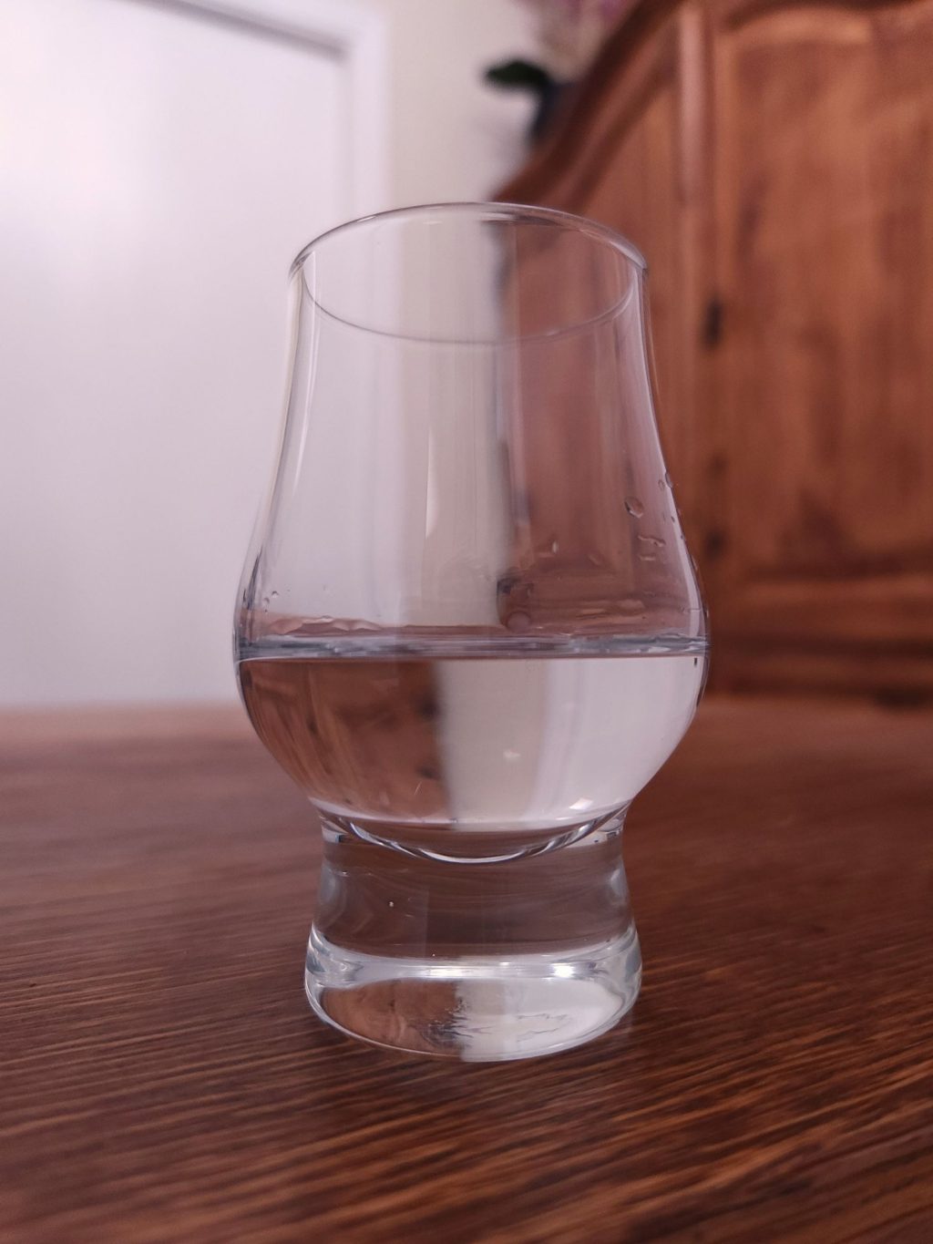 Glencairn glass with clear liquid, sitting on a wooden table
