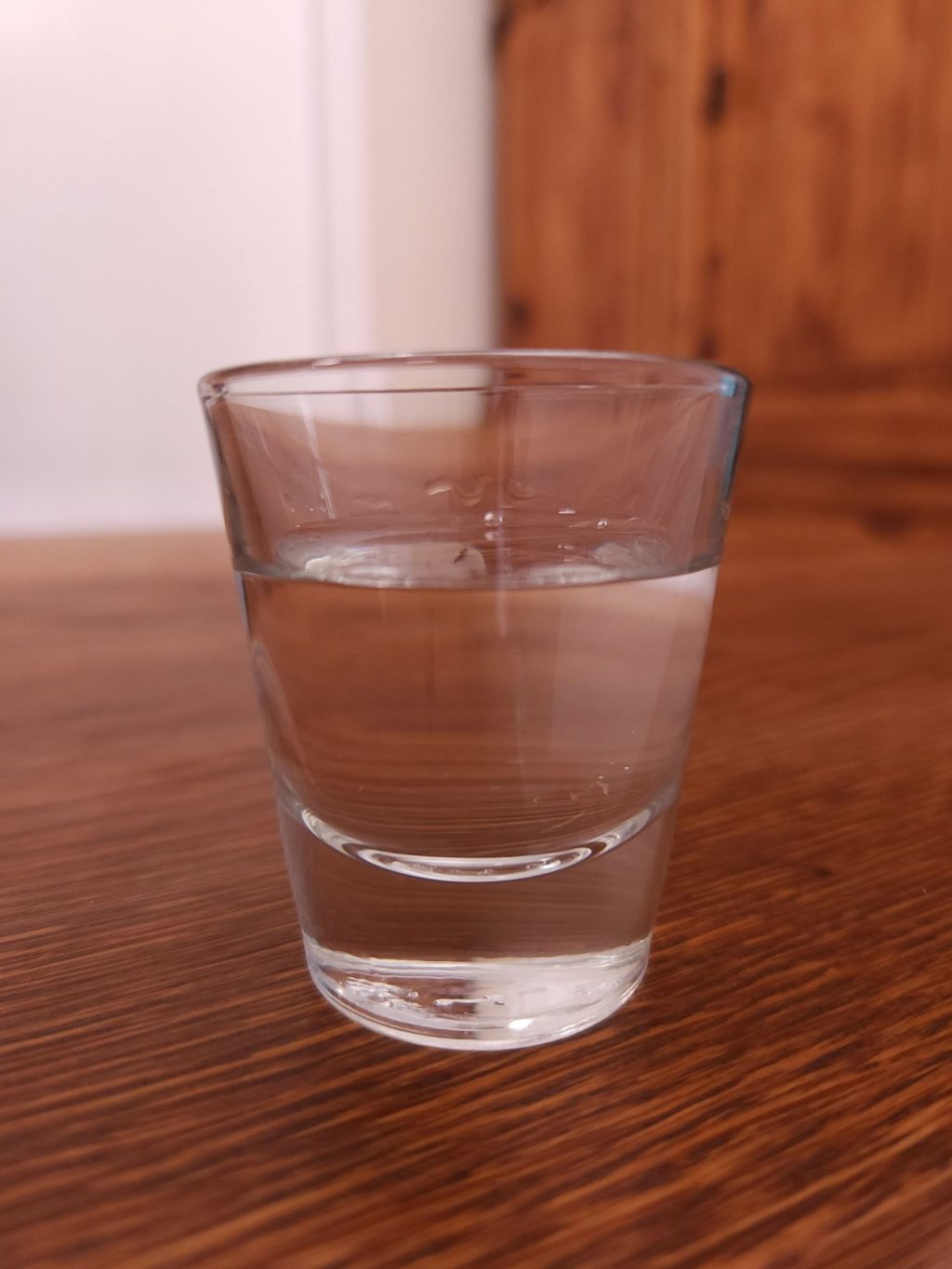 Shot glass filled with clear liquid, sitting on a wooden table