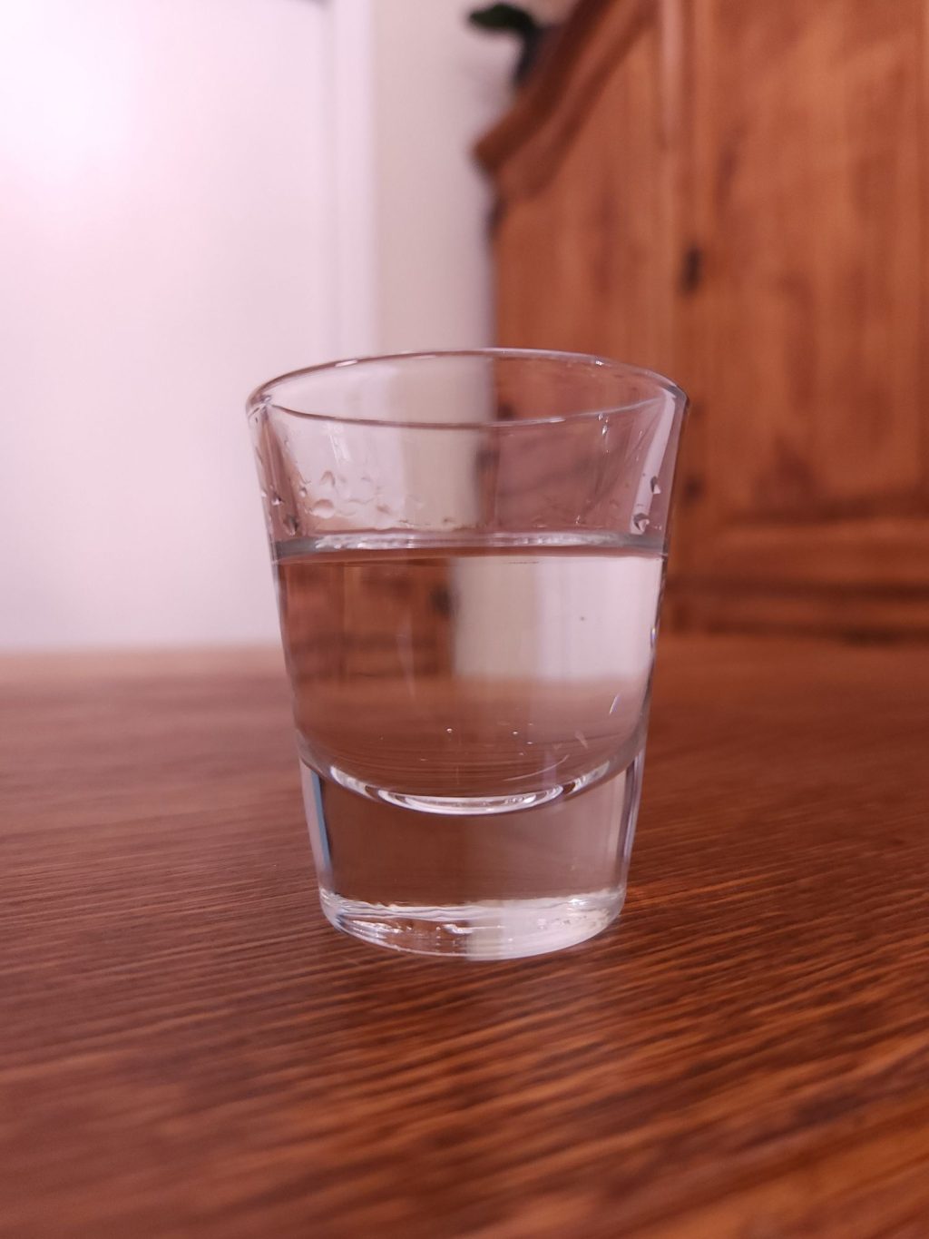 Shot glass with clear liquid, sitting on a wooden table