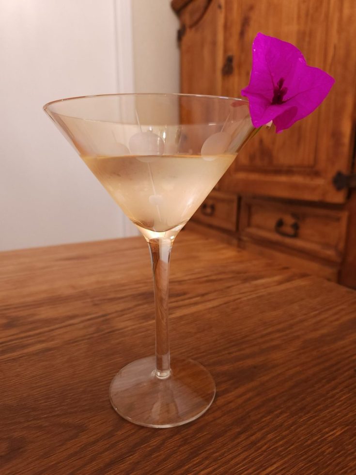 light yellow martini glass with clear liquid and a bougainvillea blossom garnish