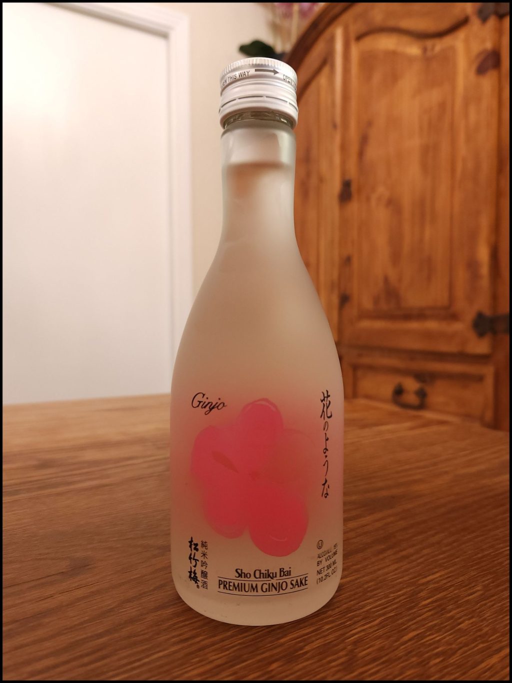 Bottle of Sho Chiky Bai Premium Ginjo Sake with a frosted glass bottle and pink and black label design, sitting on a wooden table